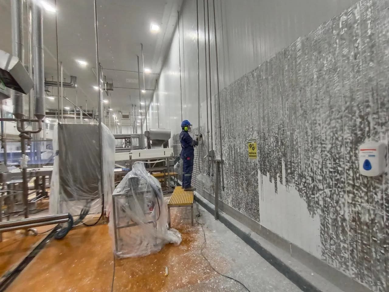 Operario aplicando pintura en planta de alimentos operativa con EPP completo